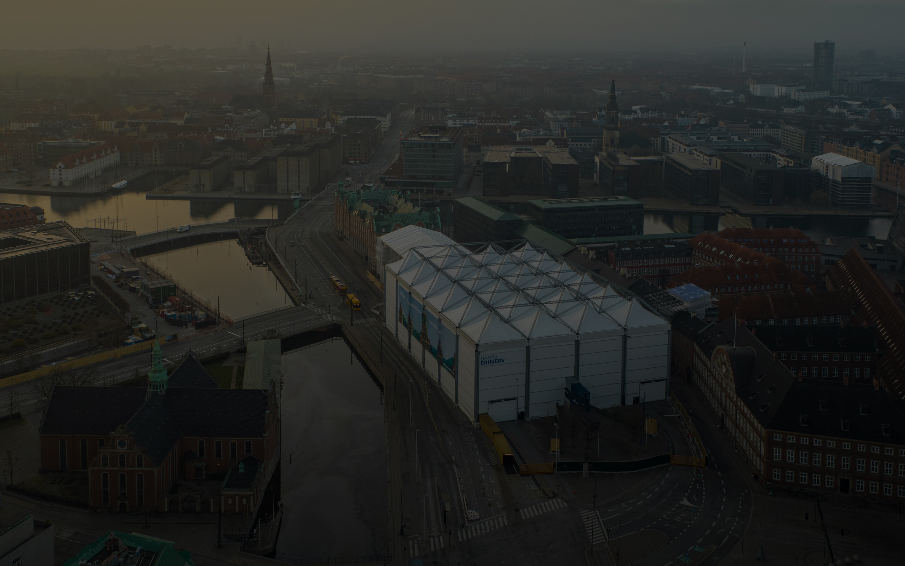 Aerial view of a copenhagen at sunrise with a large white industrial-style building near canals and historic architecture.